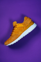 Photo of a fashionable trendy modern yellow suede women streetstyle sneaker on a violet background