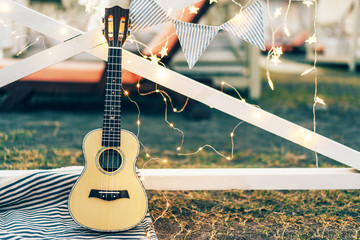 Musical instrument guitar ukulele on a festive background with lights from the garland, a summer festival picnic of ethnic music, a place for text.