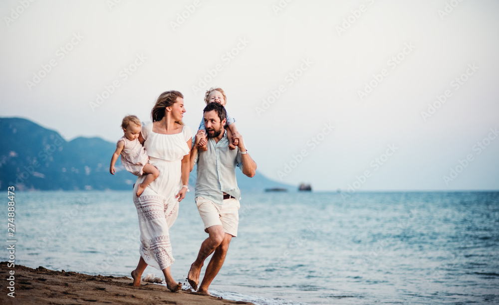 Wall mural young family with two toddler children walking on beach on summer holiday.