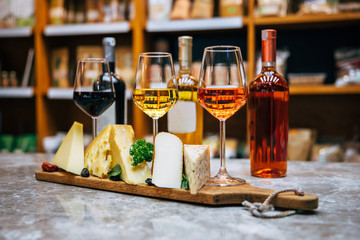 Glasses of Wine and cheese. Assortment or various type of cheese, wine glasses and bottles on the table in restaurant. Red, rose and yellow wine or champagne on the table. Winery concept image