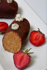 Potato cake decorated with cream. Visible slice of cake. Nearby are the halves of strawberries for decoration.