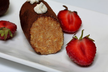 Potato cake decorated with cream. Visible slice of cake. Nearby are the halves of strawberries for decoration.
