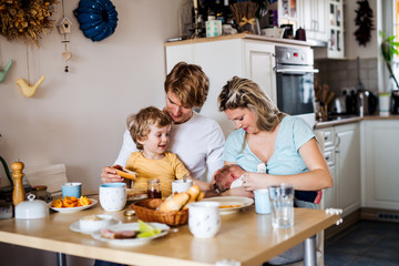 Young parents with newborn baby and small toddler son at home.