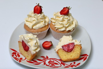 Cupcakes with strawberries and butter cream. One is cut in half. Visible filling.