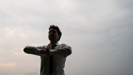 Young businessman standing under cloudy sky meditating
