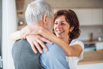Affectionate senior couple in love standing indoors at home, hugging.