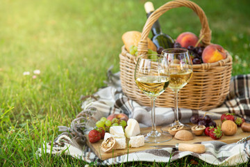 Picnic setting with  white wine,  cheese, fruits and nuts. Outdoor dinner on a  green lawn