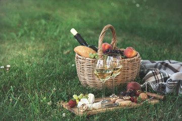 Picnic setting with  white wine,  cheese, fruits and nuts. Outdoor dinner on a  green lawn - obrazy, fototapety, plakaty