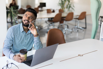 Young indian business male on laptop and coffee in modern office