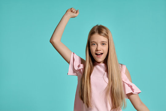 Studio portrait of a beautiful girl blonde teenager in a pink t-shirt posing over a blue background.