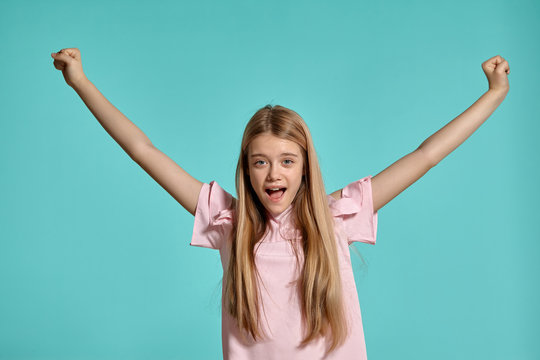 Studio portrait of a beautiful girl blonde teenager in a pink t-shirt posing over a blue background.
