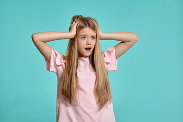 Studio portrait of a beautiful girl blonde teenager in a pink t-shirt posing over a blue background.