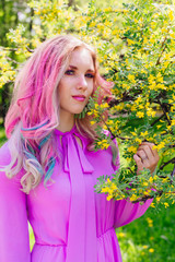 Beautiful girl with colorful dyed hair and perfect makeup and hairstyle standig next blooming barberry bush with yellow flowers