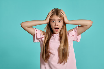 Fototapeta premium Studio portrait of a beautiful girl blonde teenager in a pink t-shirt posing over a blue background.