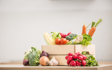 Wooden box full of fresh healthy vegetables. Broccoli carrot radish onion garlic corn on wooden kitchen table