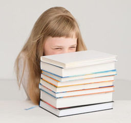 The girl with sly squint looks at a pile of books