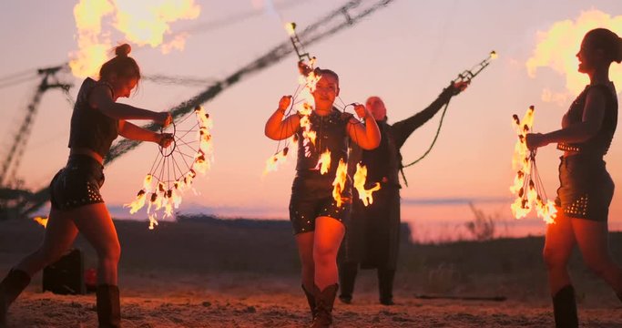 A group of professional circus performers with fire shows dance shows in slow motion using flame-throwers and rotating the torches burning objects.
