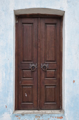 Closed double-leaf vintage door. Old wooden shabby door with bizarre metal door handles, stucco wall. Symmetric front view from outside