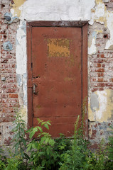 Closed old painted metal door. Symmetric front view from outside, old brick wall, brown shabby paint 