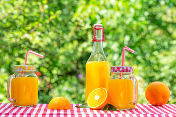 Bottle and cans of orange juice with oranges on checkered tablecloth
