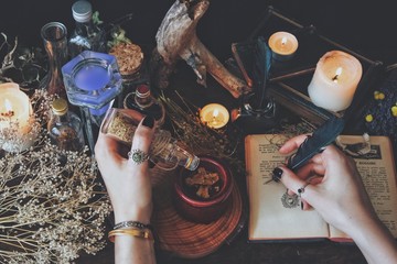 A witch casting a spell and writing it down in her Book of Shadows with a green black feather and...