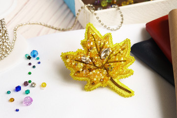 Handmade beaded brooch yellow maple leaf on table on white background