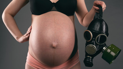 Pregnant woman is holding a gas mask on a gray background. Toxicosis concept.