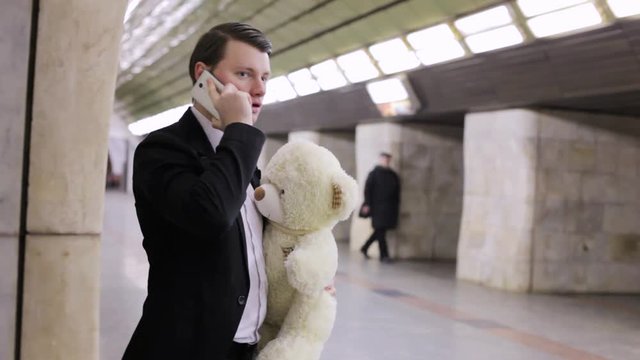 Man is talking on the phone and is waiting for his beloved, in his hand is a gift toy bear.