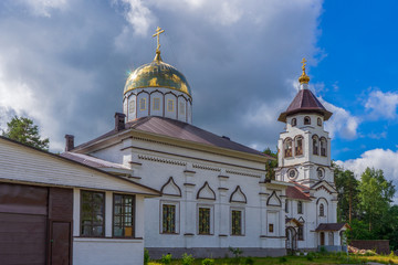 Fototapeta na wymiar Church to St. Grand Prince Alexander Nevsky in Pudozh after restoration. Orthodox temple and bell tower against northern pine forest and blue sky in summer sunny day. Karelia, Russia
