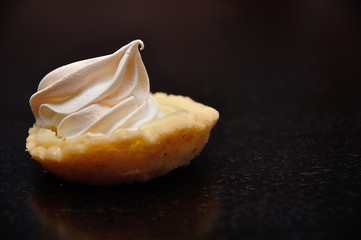 A small lemon meringue tart on a black background