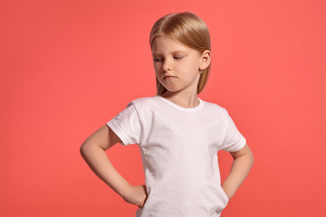 Fototapeta premium Close-up studio shot of a nice blonde little girl in a white t-shirt posing against a pink background.