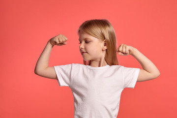 Close-up studio shot of a nice blonde little girl in a white t-shirt posing against a pink...