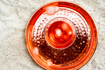 Glass of aperol spritz with ice on copper tray on sand background outdoors