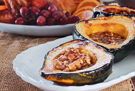Baked acorn squash with walnuts served for Thanksgiving Day dinner with roast stuffed turkey blurred in background.