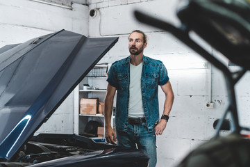 Portrait of attractive Caucasian man posing near his old vintage retro car in a garage