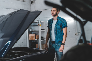 Portrait of attractive Caucasian man posing near his old vintage retro car in a garage