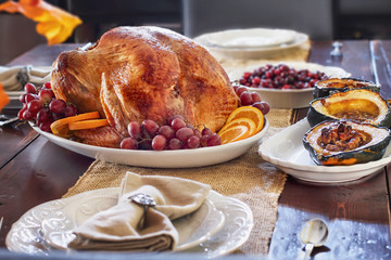 Delicious golden roasted Thanksgiving turkey on a platter garnished with fresh grapes and slices of oranges on a rustic farmhouse table.