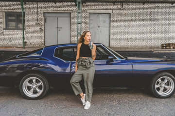 Beautiful Caucasian female posing with an old classic retro muscle car. Automotive lifestyle