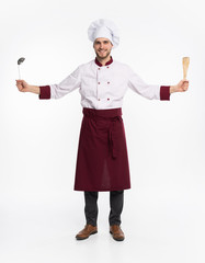 Positive toothy chef cook in beret, white outfit having tools in crossed arms looking at camera isolated on white background.