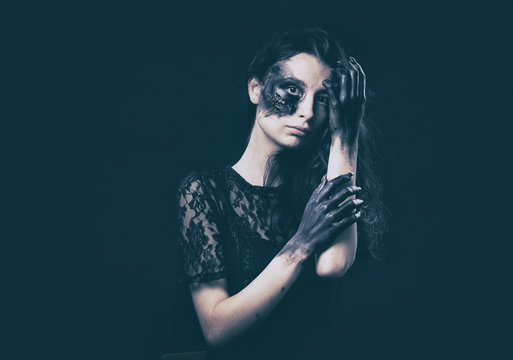 a young succubus girl on a smoke background with hands stained with soot and a burned face with an expressive look and a pleasant appearance in a black dress
