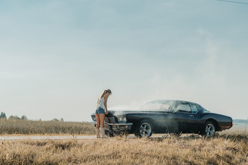 Fototapeta na wymiar Young female standing near overheated car in the field, bright sunlight, steam under the hood