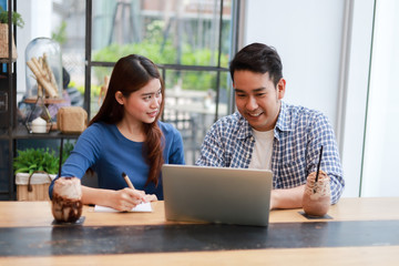 Asian couple in blue shirt drinking coffee talking and working with computer laptop smile and  happy mood in coffee shop cafe
