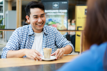 Fototapeta premium Asian couple in blue shirt drinking coffee talking and working with computer laptop smile and happy mood in coffee shop cafe