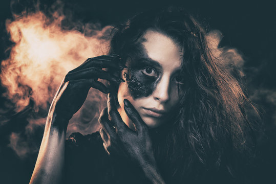 a young succubus girl on a smoke background with hands stained with soot and a burned face with an expressive look and a pleasant appearance in a black dress