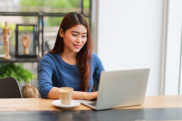 Naklejka premium Asian woman drinking coffee and working with laptop computer in cafe