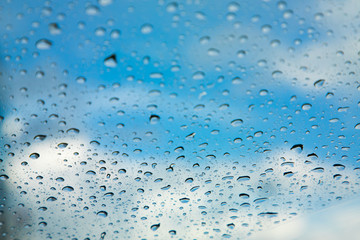 Rain drops, water drops of rain on a window glass. blurred lights city with sky clouds in rainy day, abstract blue background texture, view beautiful from outside window