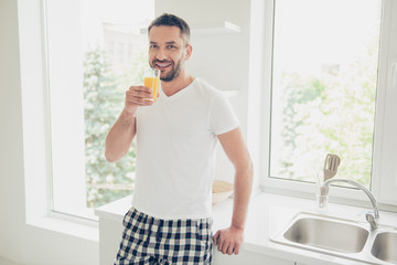 Fototapeta premium Close up photo fall asleep he him his attractive guy vacation sunday saturday arm hand orange juice glass energy refreshment white nightwear t-shirt checkered pants bright kitchen room indoors