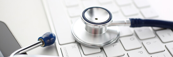 Medical stethoscope head lying on silver keyboard at doctor office worktable