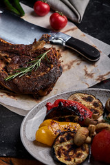 Tomahawk steak with vegetables and a knife on the table. Grilled meat with grilled vegetables and...