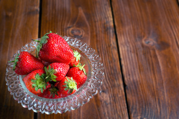 ripe strawberry in glass bowl at wooden table.